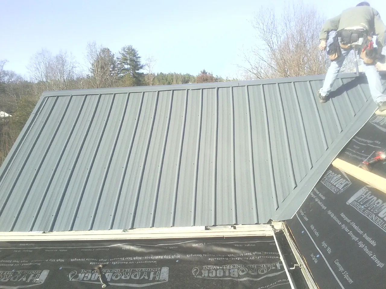 Crew installing dark green standing seam panels over synthetic underlayment in Washington